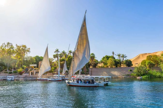 Traditional white-sailed felucca boats gliding on the blue water during a scenic Nile River Cruise in Aswan, Egypt