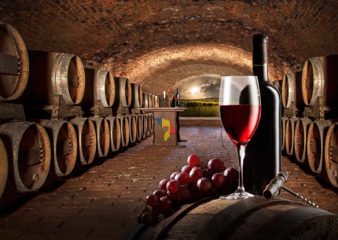 A wine bottle, a glass of red wine, and grapes sitting on a wooden barrel inside an atmospheric cellar, perfect for a Moldova wine tasting experience.