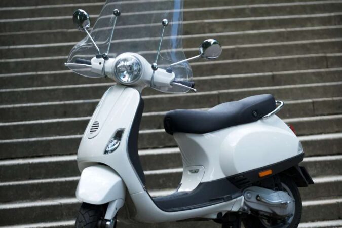 A clean white scooter parked in front of stone steps, featuring a tall transparent motorcycle screens accessory.